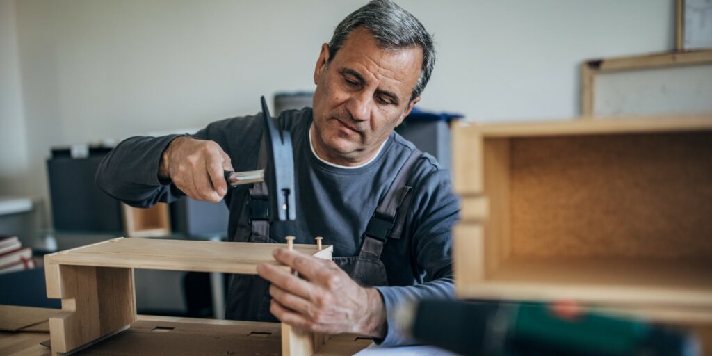One senior carpenter in work suit using hammer to make wooden drawer